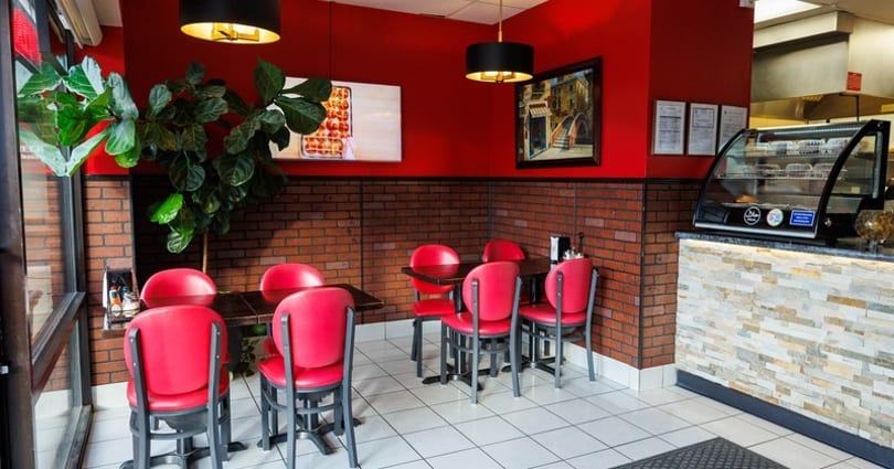Restaurant interior with red walls, brick wainscoting, red chairs, dark tables, and a display case.